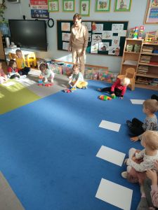 Na dywanie siedzi nauczycielka i dzieci. Troje dzieci buduje z klocków domki