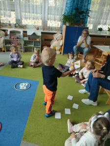 Dzieci siedzą w kole na dywanie. Chłopiec pokazuje obrazek z parasolką.