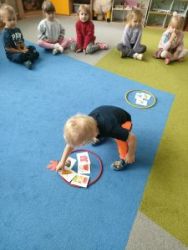 Dzieci siedzą w kole na dywanie. Chłopiec wybiera obrazek z parasolką.