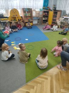 Dzieci siedzą na dywanie na którym leżą obrazki jabłek i gruszek