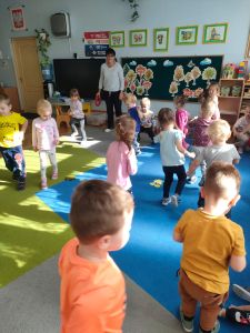 Dzieci chodzą po dywanie w rytm muzyki a na podłodze leżą liście z papieru