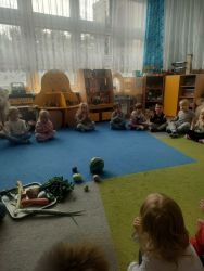 Dzieci siedzą w kole i patrzą na warzywa