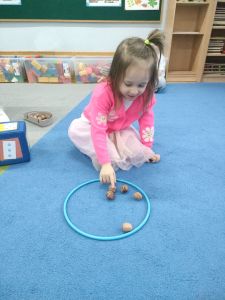 Dziewczynka liczy orzechy położone w ringu na dywanie