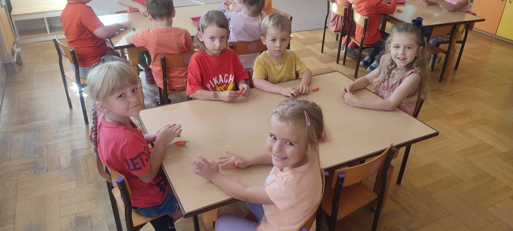 Dzieci z grupy 4 siedzą przy stolikach i lepią marchewki z plasteliny