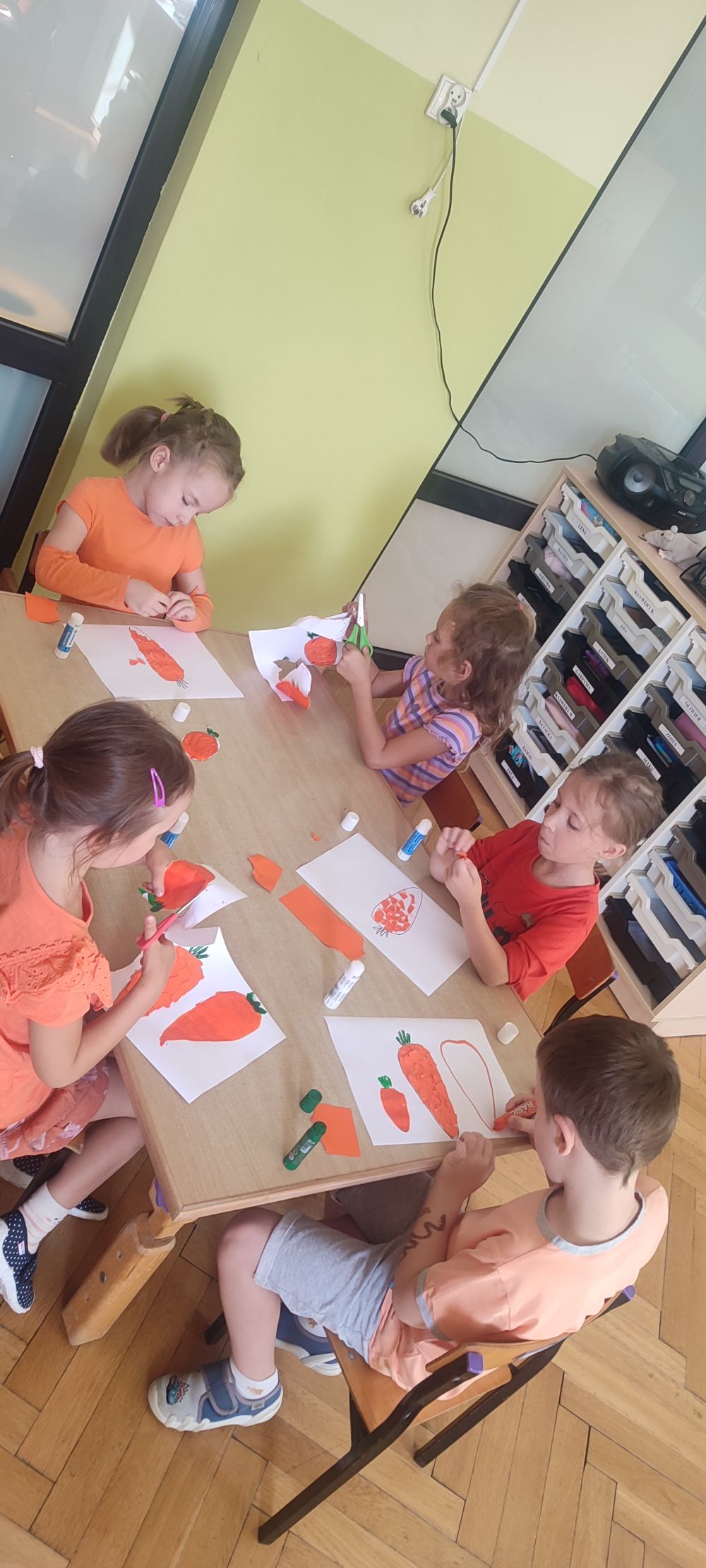 dzieci z grupy 5 wykonują pracę plastyczną przy stoliku. Malowanie marchewki, wycinanie, wylepianie kawałkami papieru