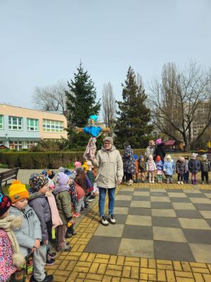dzieci stoją na przedszkolnym placu zabaw, nauczycielka trzyma w rękach marzannę