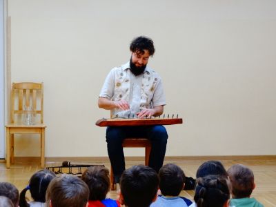 Dzieci słuchają opowieści Pana Szymona, który gra na instrumencie