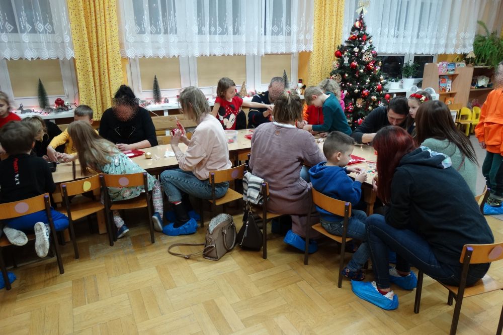 Dzieci z grupy 4 siedzą przy stolikach z rodzicami i wykonują ozdoby bożonarodzeniowe