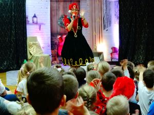 Na scenie stoi Pani Mikołajowa. Dzieci siedzą na dywanie.