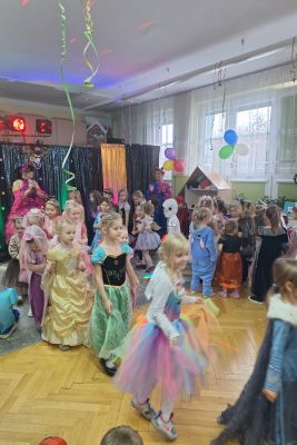 Dzieci przebrane w różne karnawałowe stroje tańczą.