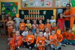 Zdjęcie grupowe grupy 4. Dzieci ubrane na pomarańczowo, na dywanie stoją koszyki z marchewkami