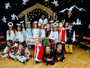 W tle dekoracja świąteczna- na ciemnym materiale stajenka Betlejemska, aniołki i gwiazdy. Zdjęcie grupowe z Dzieci z Panią Dyrektor i przedstawicielkami władz. Dzieci ubrane w stroje pasterzy, aniołków, Maryi, Józefa, Królów i w stroje ludowe.
