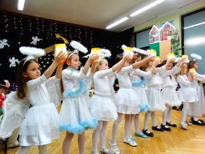 W tle dekoracja świąteczna- na ciemnym materiale stajenka Betlejemska, aniołki i gwiazdy. Dzieci ubrane w stroje pasterzy, aniołków, Maryi, Józefa, Królów i w stroje ludowe. Na środku sceny dziewczynki w strojach aniołów tańczą taniec z lampionami