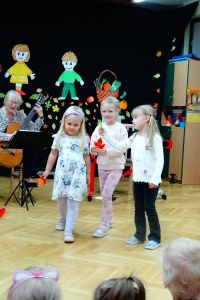 Pani gra na gitarze, a 3 dziewczynki idą z listkami w ręku