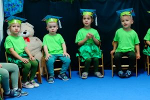 Dzieci ubrane na zielono siedzą na krzesełkach