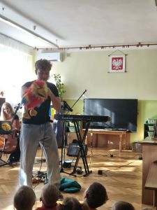 Dzieci siedzą i słuchają koncertu, Na scenie Pan trzymający pluszową papugę i i Pani grająca na wiolonczeli