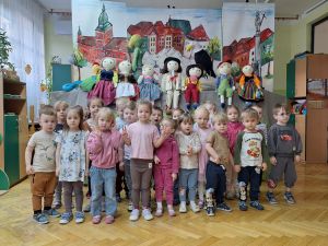 Zdjęcie grupowe grupy 1. W tle dekoracja z przedstawienia- kukiełki i namalowane miasto