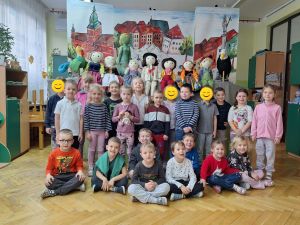 Zdjęcie grupowe grupy 5. W tle dekoracja z przedstawienia- kukiełki i namalowane miasto
