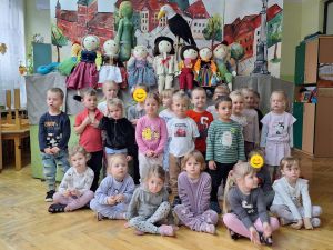 Zdjęcie grupowe grupy 2. W tle dekoracja z przedstawienia- kukiełki i namalowane miasto