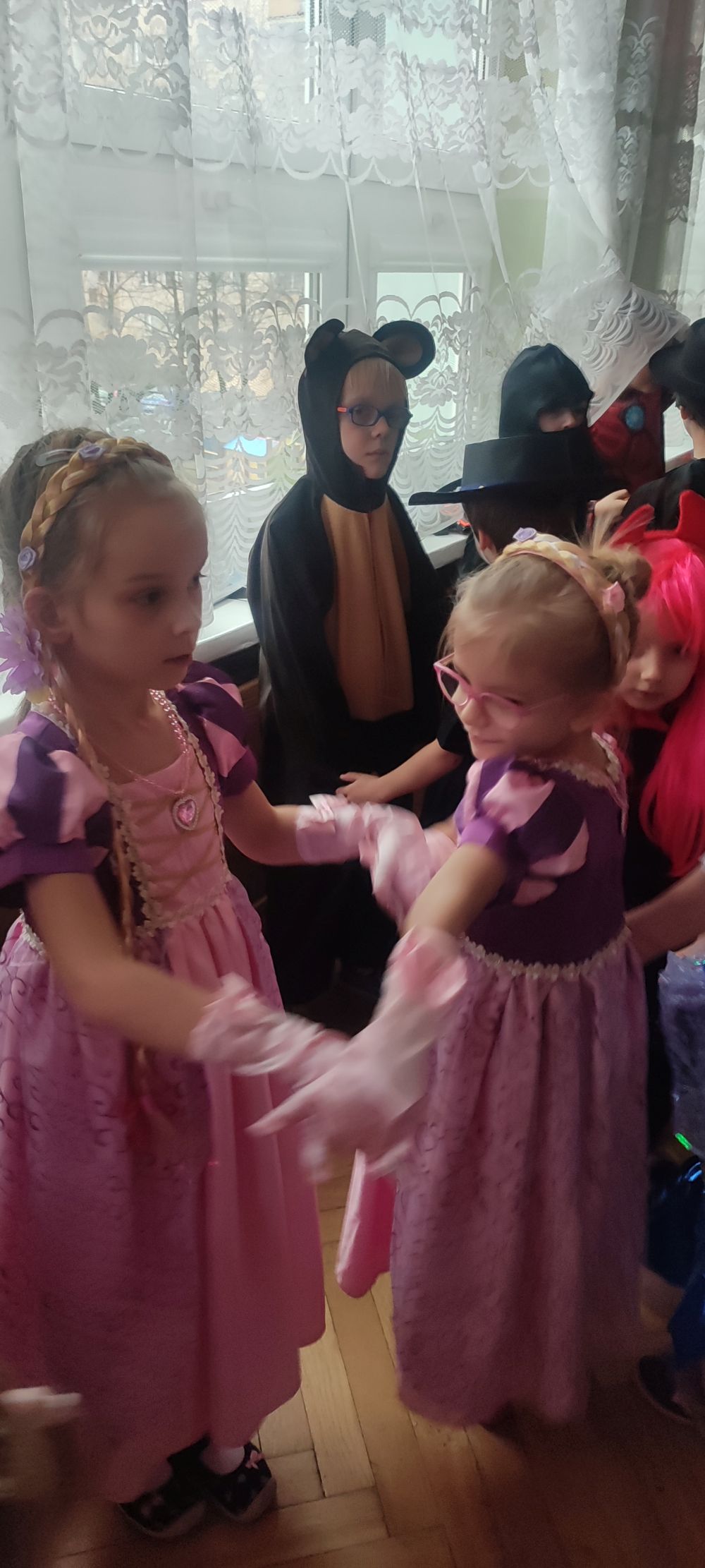 Dzieci tańczące na balu karnawałowym. Na pierwszym tle dwie dziewczynki w stroju roszpunki i chłopiec w stroju misia