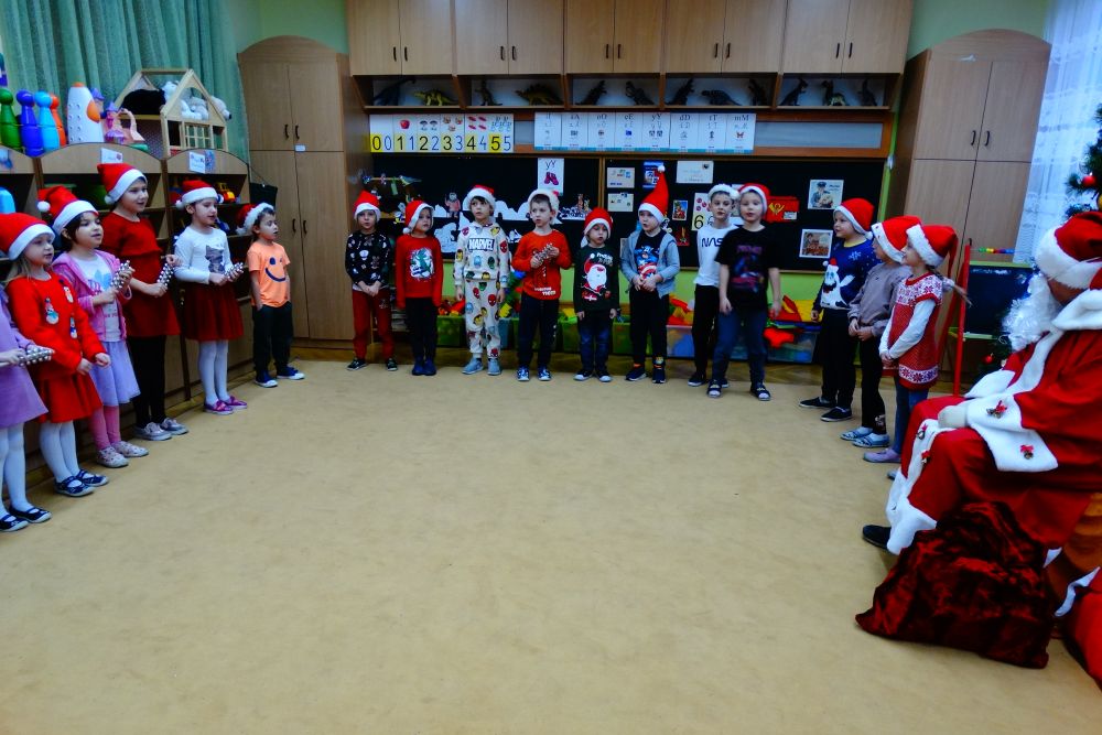 Dzieci stoją w półkolu grając na instrumentach w rytm piosenki śpiewanej Mikołajowi