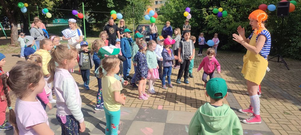 Dzieci stoją na przedszkolnym placu zabaw przodem do pani przebranej za Pippi