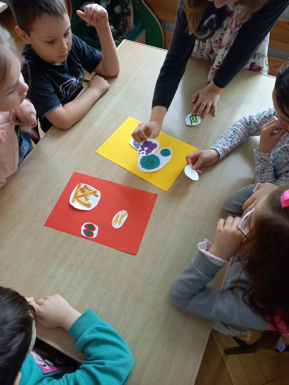 Dzieci siedzą przy stoliku i układają na kolorowych kartkach obrazki wirusów i bakterii