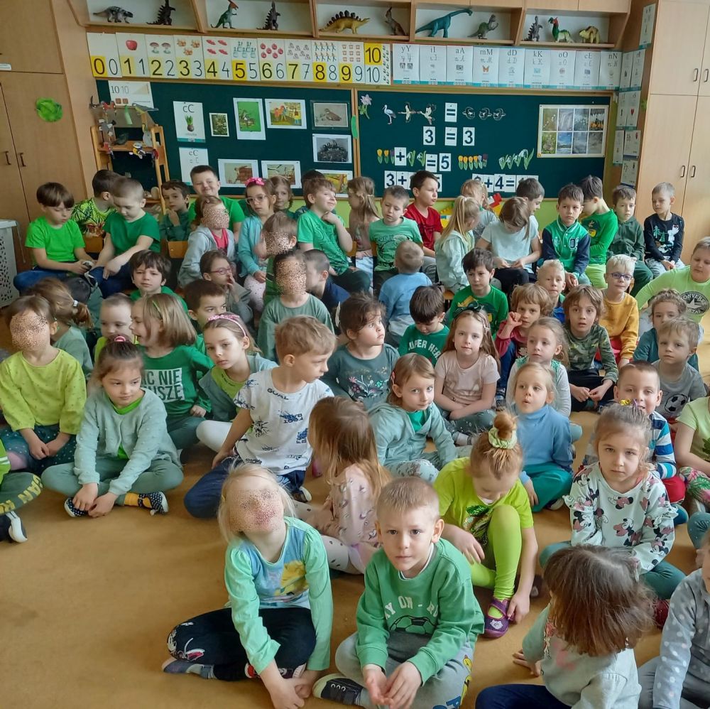 Dzieci ze wszystkich grup siedzą na dywanie. dzieci ubrane są na zielono