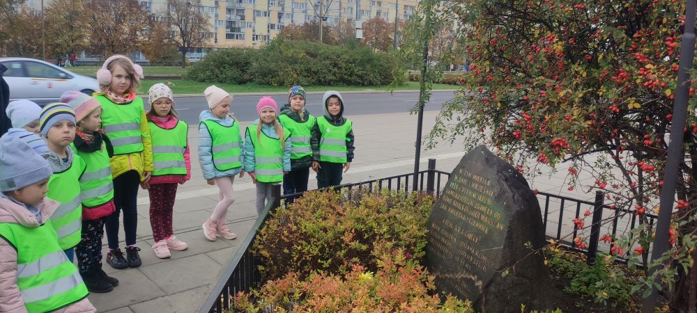 Dzieci z grupy 4 stoją przed pomnikiem poległych w walce sanitariuszek i harcerek