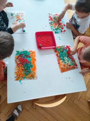 Dzieci stemplują na kartkach papieru kolorowe kropki w barwach jesiennych