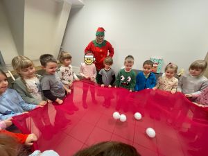Dzieci trzymają czerwoną chustę, na środku której leżą białe styropianowe kule