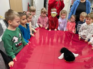 Dzieci trzymają czerwoną chustę, na środku której leży pluszowy pingwin