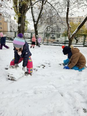 Dzieci bawią się w śniegu, toczą kule na bałwana