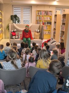 Dzieci siedzą na krzesłach, przodem do dzieci siedzi Pani na kanapie ubrana w strój elfa