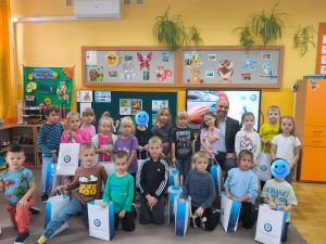 Zdjęcie grupowe dzieci z Tatą Ewy. Dzieci mają w rękach torby z prezentami od firmy PZU