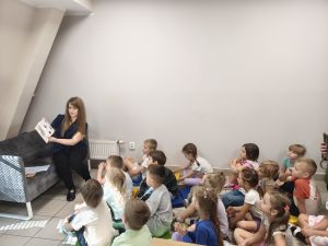 Pani bibliotekarka czyta dzieciom książkę, dzieci siedzą na dywanie