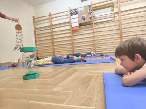 Dzieci leżą na matach i patrzą na przesypujący się piasek w klepsydrze