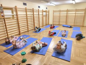 Dzieci leżą na matach i robią kołyskę, leżąc na brzuchu i trzymając się za kostki