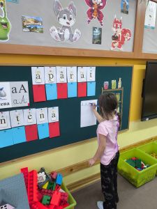 Dziewczynka stoi przy tablicy i pisze wielką literę A