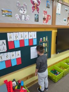 Chłopiec stoi przy tablicy i pisze wielką literę A