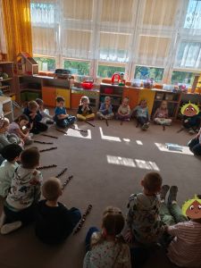 Dzieci siedzą na dywanie, przed każdym dzieckiem leżą kasztany ułożone w kolumnie