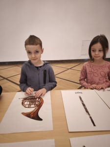 Chłopiec i dziewczynka stoją przy stole a przed nimi leżą karty  z obrazkami instrumentów