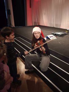 Chłopiec gra smyczkiem na skrzypcach, które trzyma Pani