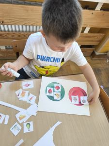 Chłopiec przykleja wycięte obrazki na kolorowych talerzach