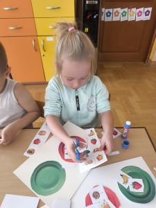 Dziewczynka przykleja wycięte obrazki na kolorowych talerzach