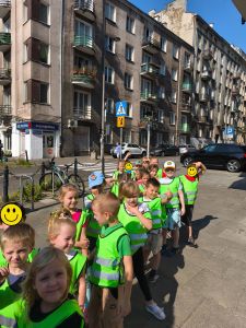 Dzieci stojące w parach a za nimi ulica i znaki drogowe