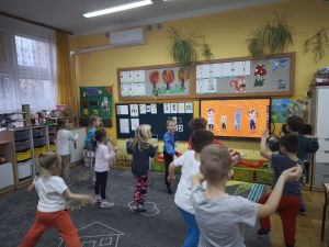 Dzieci tańczą zumbę na dywanie naśladując ruchy postaci z telewizora