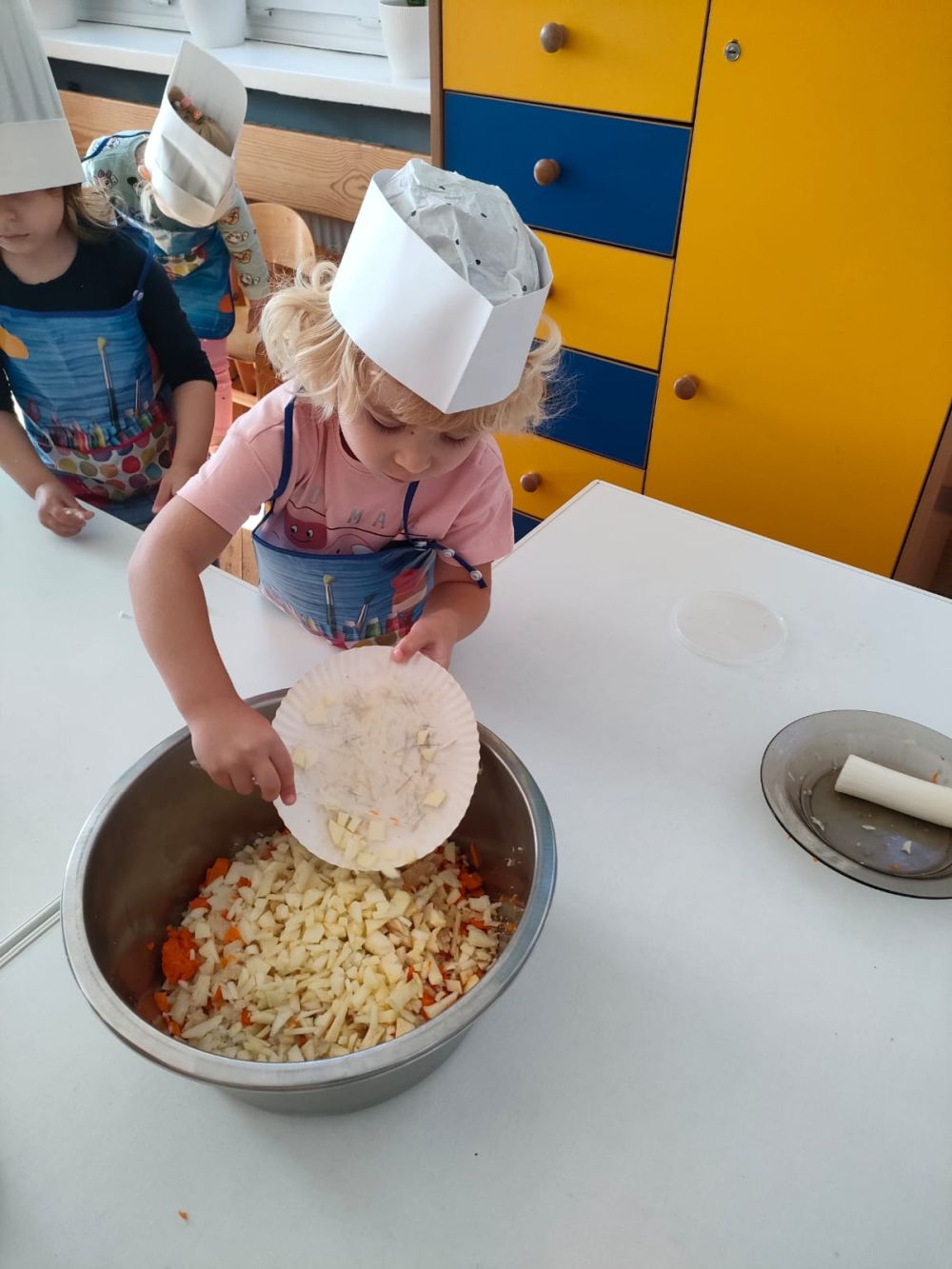 dziewczynka w stroju kucharza zrzuca z talerzyków pokrojone warzywa