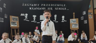 Dzieci siedzą a jeden chłopiec stoi i mówi wiersz