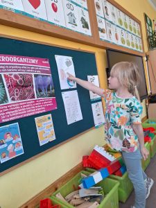 Dziewczynka pokazuje palcem obrazek na kartce wiszącej na tablicy w sali